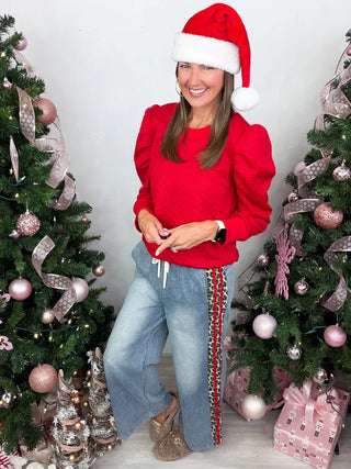 Person wearing a red sweater and Santa hat in front of Christmas trees with pink ornaments.