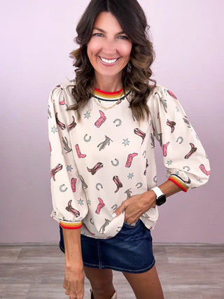 Woman wearing a blouse with cowboy boot and horseshoe pattern against a light purple background